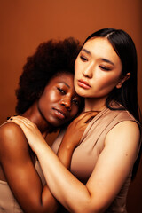 young pretty asian, african american woman posing cheerful together on brown background, lifestyle diverse nationality people concept