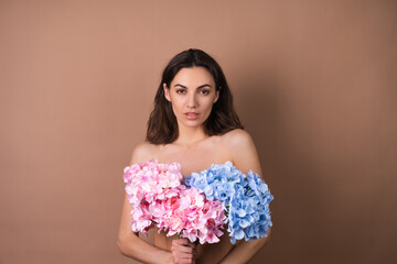 Beauty portrait of a topless woman with perfect skin and natural make-up on beige background holding bouquet of colorful flowers
