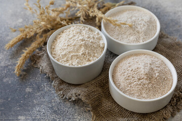 Food and baking ingredient. Wheat flour coarse from whole wheat grains, wheat bran and wheat flour over gray stone background. Copy space.