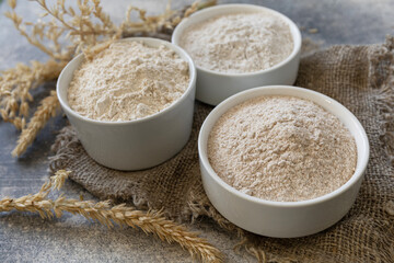 Food and baking ingredient. Wheat flour coarse from whole wheat grains, wheat bran and wheat flour over gray stone background.