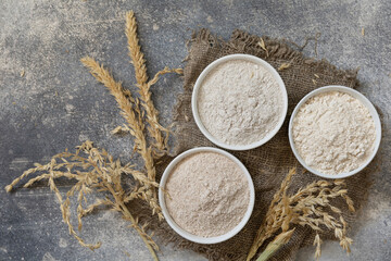 Food and baking ingredient. Wheat flour coarse from whole wheat grains, wheat bran and wheat flour over gray stone background. Top view flat lay.