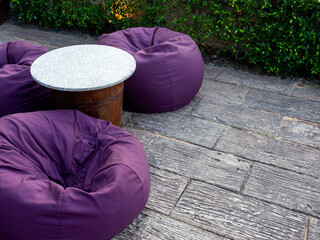Empty round marble top table with three purple bean bags with copy space on the ground near the...