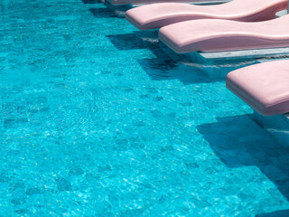 The empty retro style of pink color curved sunbeds, chairs on the blue swimming pool in a hotel...