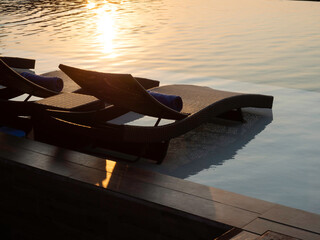 Two empty modern rattan sunbeds, bed chairs for guests on white marble floor at the pool in hotel...