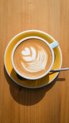 Speciality coffee cup with art latte depicting a heart shaped flower served on a wooden table