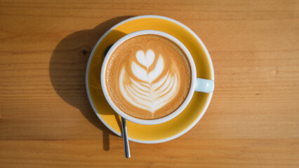 Speciality coffee cup with art latte depicting a heart shaped flower served on a wooden table