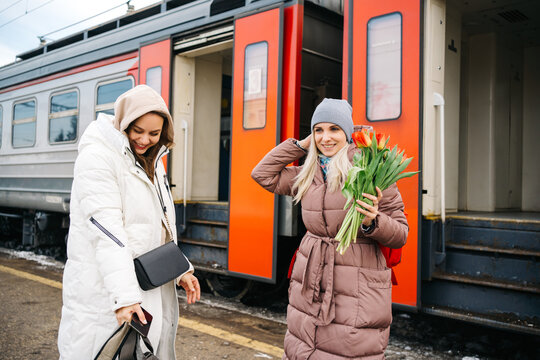 joyful girls with flowers on the platform of the station