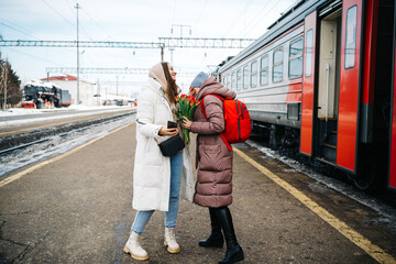 girls with flowers say goodbye on the platform of the station