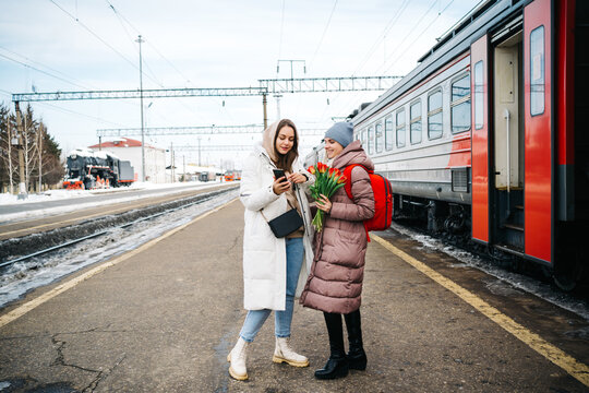 two girls on the station platform with flowers happily looking into a smartphone