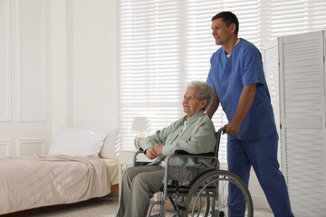 Fototapeta na wymiar Caregiver assisting senior woman in wheelchair indoors. Home health care service