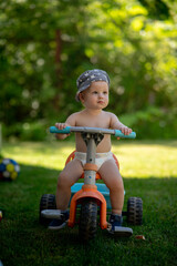Cute toddler with blue hat is on tricycle in summer