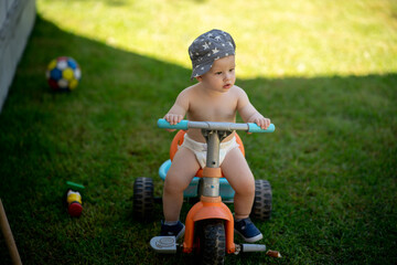 Cute toddler with blue hat is on tricycle in summer