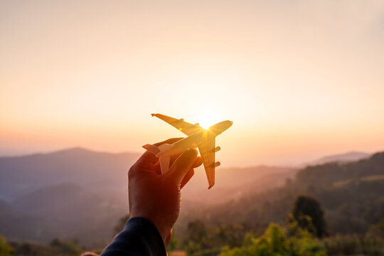 Hand holding a miniature airplane with the mountain view at sunrise, Summer vacation and travel concept