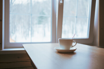 A cup on the table in front of the window.