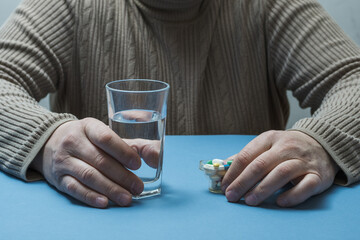 The man is holding a glass of water and pills.