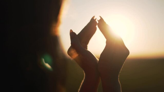 Happy girl in park at sunset. Figure made by fingers. Hands of girl shape of heart. Summer dream. Happiness of freedom in field at sunset. Sunlight between fingers. Silhouette of happy girl in park