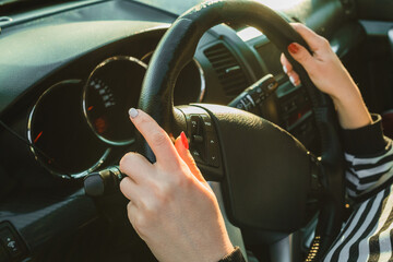 Female hands on black steering wheel of modern car. Automobile saloon. Woman driving on road. 