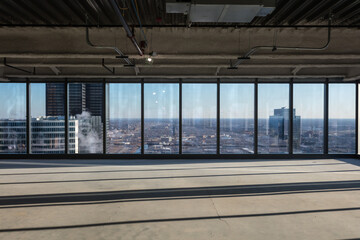 Fototapeta na wymiar Dramatic view of large urban area through floor to ceiling windows of highrise with undeveloped office space