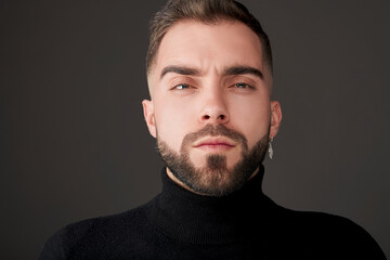 Obraz premium Male model shot in studio. Serious and confident expression. Angry or upset look and a casual style. Headshot of man with a beard, brown hair, brown eyes on a grey solid background. 