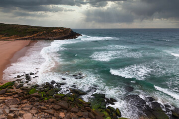 Coastal landscape with dramatic sky over the beach at sunset. View of rocky coast of the Atlantic Ocean with large waves. 