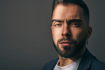 Obraz premium Male model shot in studio. Serious and confident expression. Angry or upset look and a casual style. Headshot of man with a beard, brown hair, brown eyes on a grey solid background. 