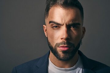 Fototapeta premium Male model shot in studio. Serious and confident expression. Angry or upset look and a casual style. Headshot of man with a beard, brown hair, brown eyes on a grey solid background. 