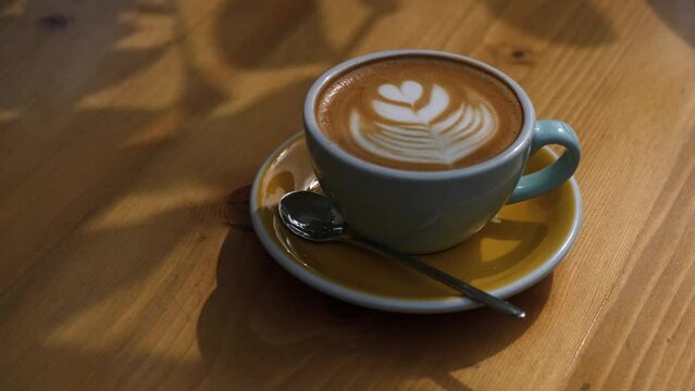 Speciality coffee cup with art latte depicting a heart shaped flower served on a wooden table
