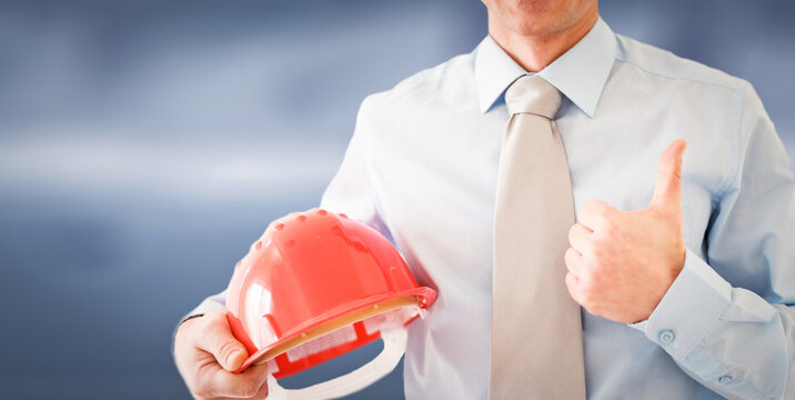 Businessman wearing a blue shirt and tie holding a helmet in his hand showing ok sign.Man in construction and engineering concept.