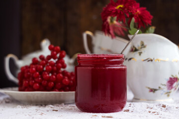 Healthy jam from viburnum berries (Viburnum opulus) in a glass jar, a bunch of viburnum, antique dishes and chrysanthemums in a vase. Preparations for the winter from colds