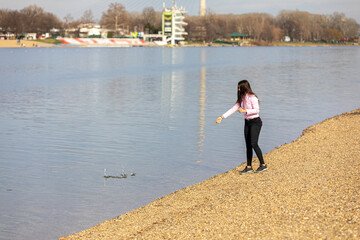 A young girl standing on the lake bank and throwing stones into the water. Recreation in nature, leisure, walks in the fresh air.