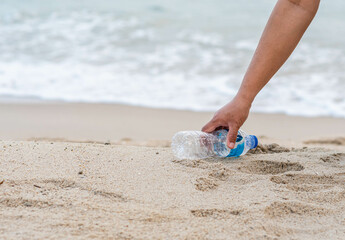 Woman cleans up by picking up plastic bottles at the beach.