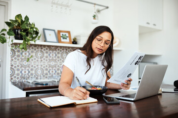 Busy building her brand from home. Shot of a young woman going through paperwork and writing notes while working from home.