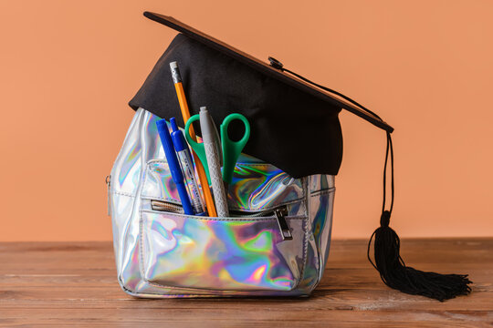 Backpack With Stationery And Graduation Hat On Wooden Table