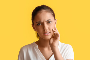 Pretty teenage girl with dental braces suffering from toothache on yellow background