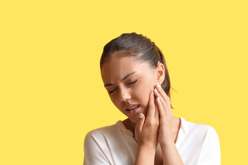 Pretty teenage girl with dental braces suffering from toothache on yellow background