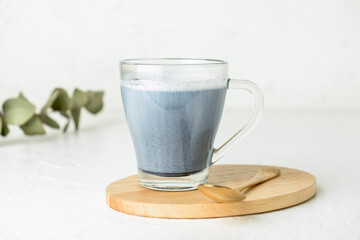 Wooden board with glass cup of delicious Charcoal Latte and spoon on light background