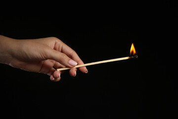 Female hand with burning fireplace match on black background