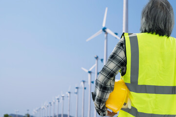 Senior male engineer holding yellow safety helmet checking wind turbine power in construction site.