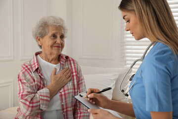 Obraz premium Young caregiver examining senior woman in room. Home health care service