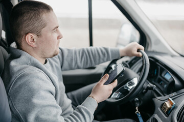male truck driver uses smartphone while sitting in cab.
