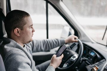 male truck driver uses smartphone while sitting in cab.