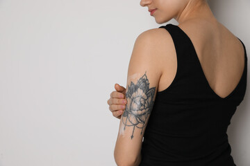 Woman applying cream onto her arm with tattoo on white background, closeup. Space for text - obrazy, fototapety, plakaty