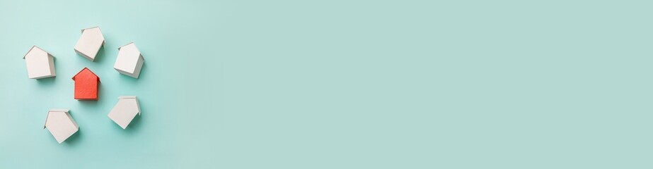 Simply flat lay design with miniature red toy model house in among white houses isolated on pastel blue background. Real estate property industry. Community unique neighborhood choice concept. Banner