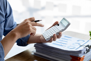 Close-up of a business man using a white calculator, a financial businessman examining the numerical data on a company financial document, he uses a calculator to verify the accuracy of numbers.