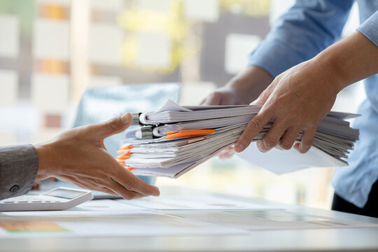 A male office worker is bringing a pile of financial documents to the head of the finance department to verify the correctness of the information before attending a meeting with the management.