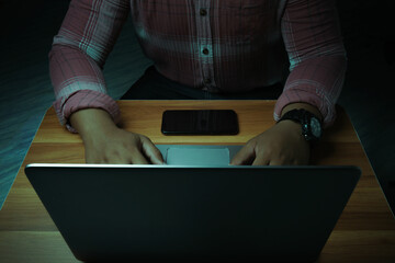 A man is sitting on a laptop in a dark room with lights shining down on it.internet concept...