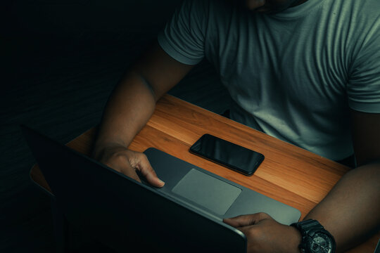 A man in a white shirt sits on a laptop in a dark room. with light shining down. internet concept addiction.topview.