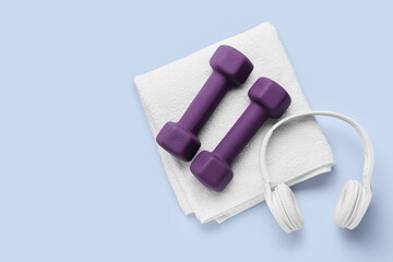 Stylish dumbbells, headphones and towel on light background