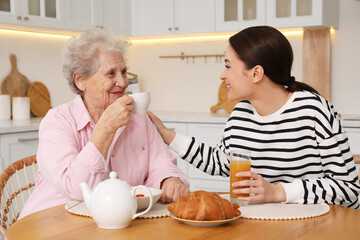 Obraz na płótnie Canvas Young caregiver and senior woman having breakfast at table in kitchen. Home care service