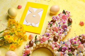 Composition with beautiful cake, painted eggs, flowers and greeting card for Easter celebration on yellow background, closeup